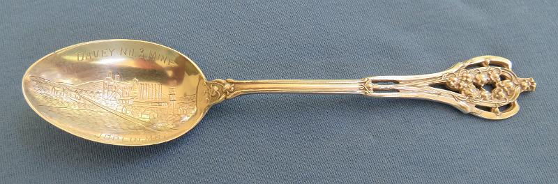Souvenir Mining Spoon Davey No. 3 Mine.JPG - SOUVENIR MINING SPOON, TRI-STATE MINING DISTRICT DAVEY NO. 3 MINE JOPLIN MO - Sterling silver spoon, 5 5/8 in. long, engraved mining scene of mine buildings in bowl, handle open design at top, bowl marked DAVEY NO. 3 MINE, JOPLIN MO. reverse marked with maker’s mark and Sterling, ca.1910  [The Davey No. 3 mine is typical of hundreds of lead and zinc mines located throughout the nearly 2500 square miles of the Tri-State Mining District. The Tri-State district was a historic lead-zinc mining district located in southwest Missouri, southeast Kansas and northeast Oklahoma. The Davey mines were operated by the American Lead, Zinc and Smelting Company with general offices in Boston, MA.  The company was incorporated on January 26, 1899 in Maine and by 1919 owned 2,160 acres of mineral land in the Joplin district and leased another 655 acres of land owned by the Davey family which included four Davey mines.  As of 1919, two of the mines were producing and two others were worked out.  The Tri-State Mining District produced lead and zinc for over 100 years. Production began in the 1850s and 1860s in the Joplin - Granby area of Jasper and Newton counties of southwest Missouri. By the turn of the century Joplin with a population of 26,000 was quickly becoming the center of the mining activity for the Tri-State Mining District. The value of Tri-State mineral production from 1850 to 1950 exceeded one billion dollars.  Until 1945, the region was rated as the leading producer of lead and zinc concentrates in the world, accounting for one-half of the zinc and ten percent of the lead produced in the United States. Production continued until the closure of the Picher, Oklahoma mines in 1967, and the Swalley mine near Baxter Springs, Kansas in 1970. The Tri-State district includes three mining-related Superfund sites: the Tar Creek Superfund site in Oklahoma; the Jasper County and Newton County sites in Missouri; and the Cherokee County site in Kansas.]